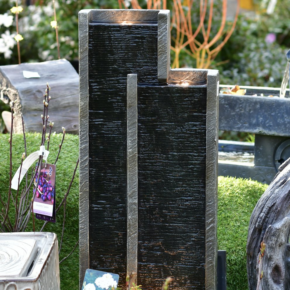 Gartenbrunnen in Form von zwei rechteckigen Türmen, die in der Mitte dunkelgrau und außen hellgrau sind.