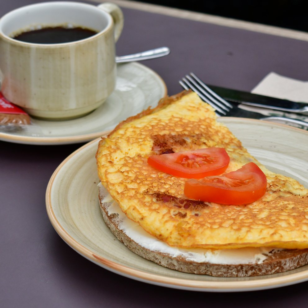 dingers-fruehstueck Ein Omelett auf einer Scheibe Brot und dahinter steht eine Tasser Kaffee