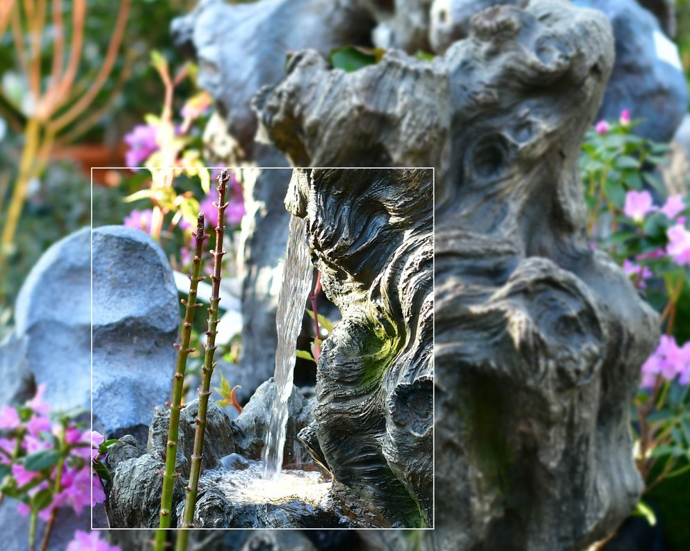 Gartenbrunnen in Organischer Form mit mehreren Stellen, an denen Wasser läuft, von Blumen umgeben