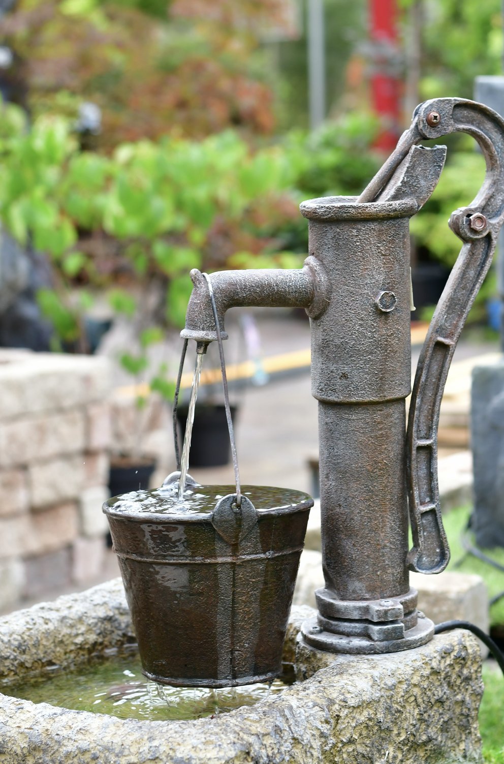Gartenbrunnen in Form einer alten Pumpe mit Eimer, in den das Wasser läuft