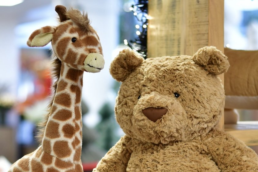 Jellycat Kuscheltiere Bär und Giraffe sitzen auf einem Holzregal