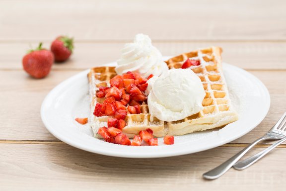 Eine eckige Waffel mit Erdbeeren, Sahne und Vanilleeis auf einem Teller