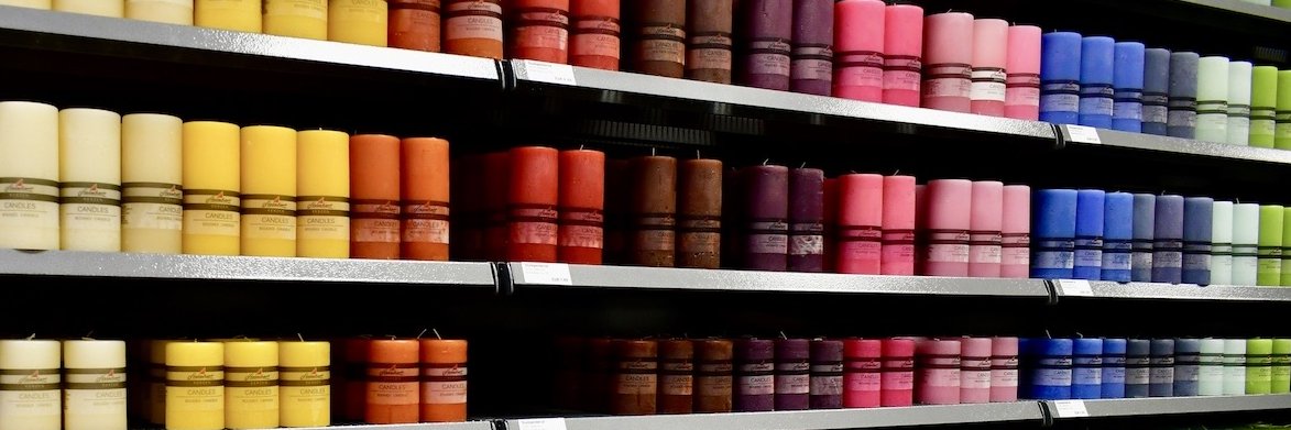 Regal mit verschiedenen Kerzen angeordnet in Regenbogen-Farben