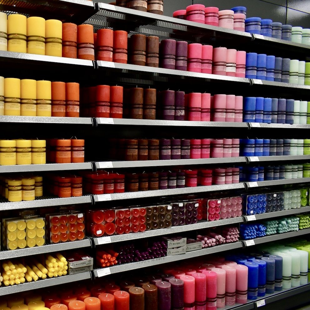 Regal mit verschiedenen Kerzen angeordnet in Regenbogen-Farben