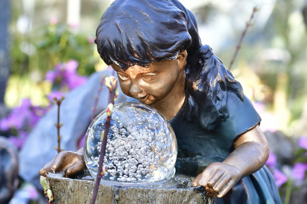 Gartenbrunnen in Form eines Mädchens, das in eine Glaskugel schaut, die sich im Wasser dreht