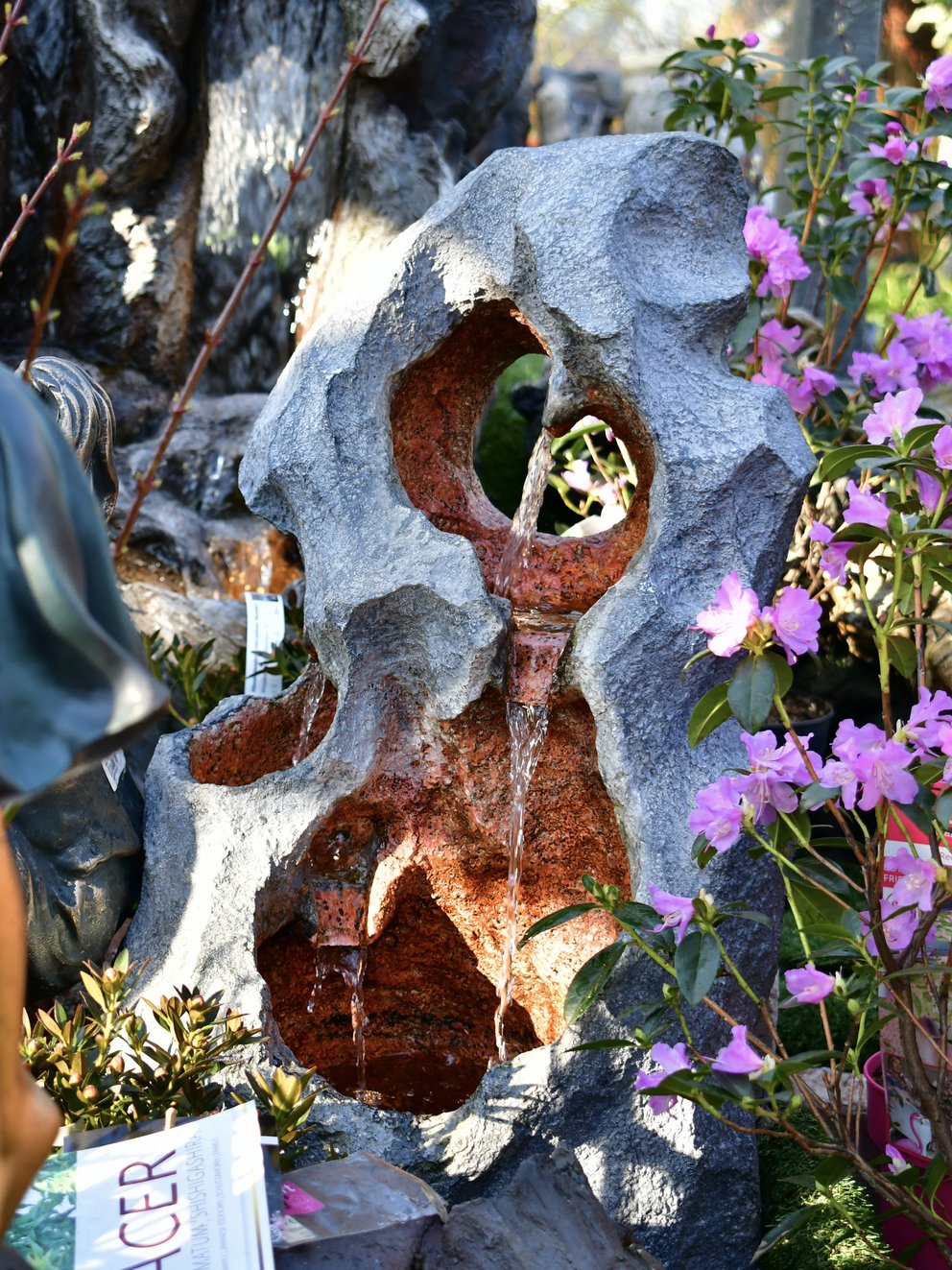 Gartenbrunnen in organischer Stein-Optik mit zwei Löchern in der Mitte, über die das Wasser läuft