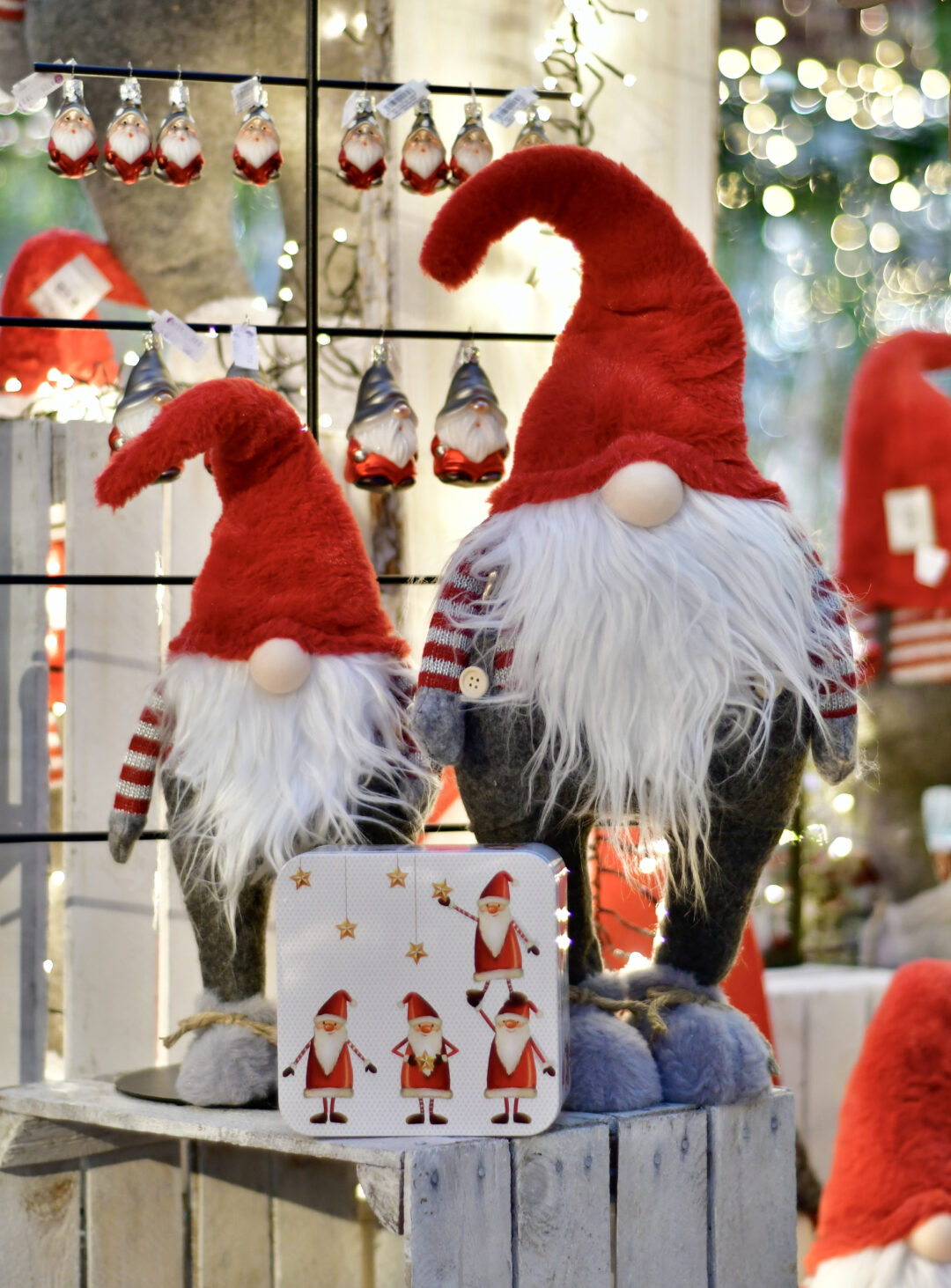 Zwei Weihnachtswichtel aus unserem Weihnachtsbazar, die auf einer weißen Holzkiste stehen. Im Hintergrund sieht man passende Weihnachtskugeln in Wichtel-Optik.