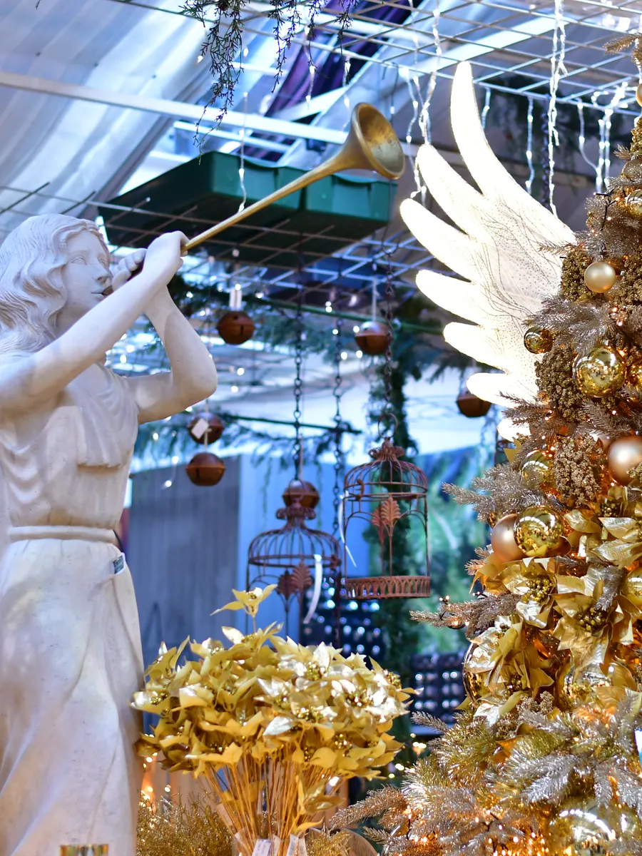Engelsfigur mit Trompete neben einem goldenen Themenbaum