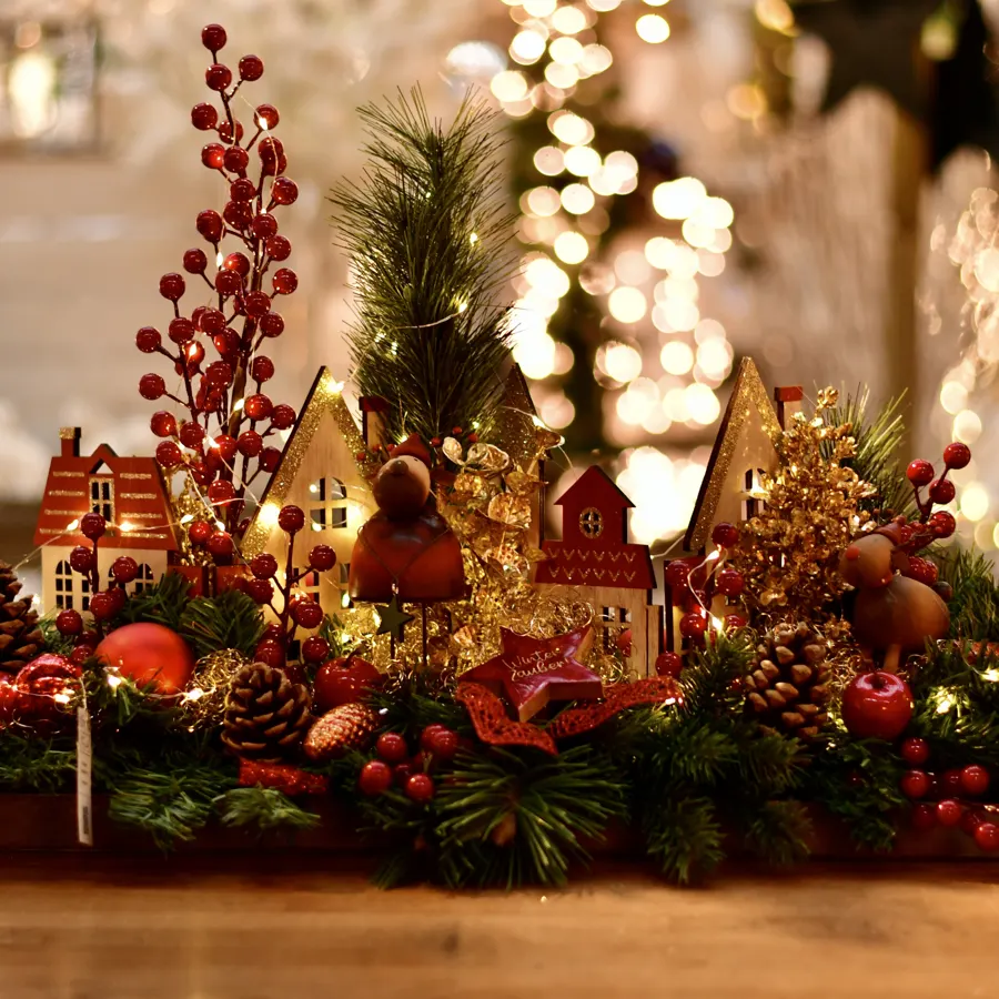 Adventsgesteck als rotes Winterdorf mit Beeren