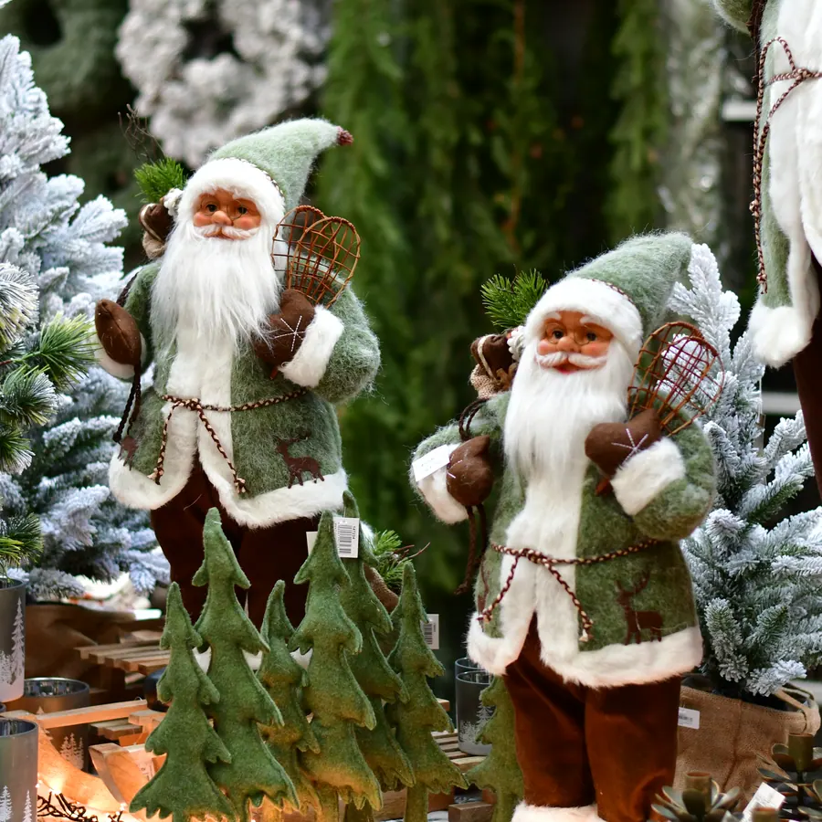 Zwei Weihnachtsmann-Figuren in Grün zwischen verschneiten Tannen