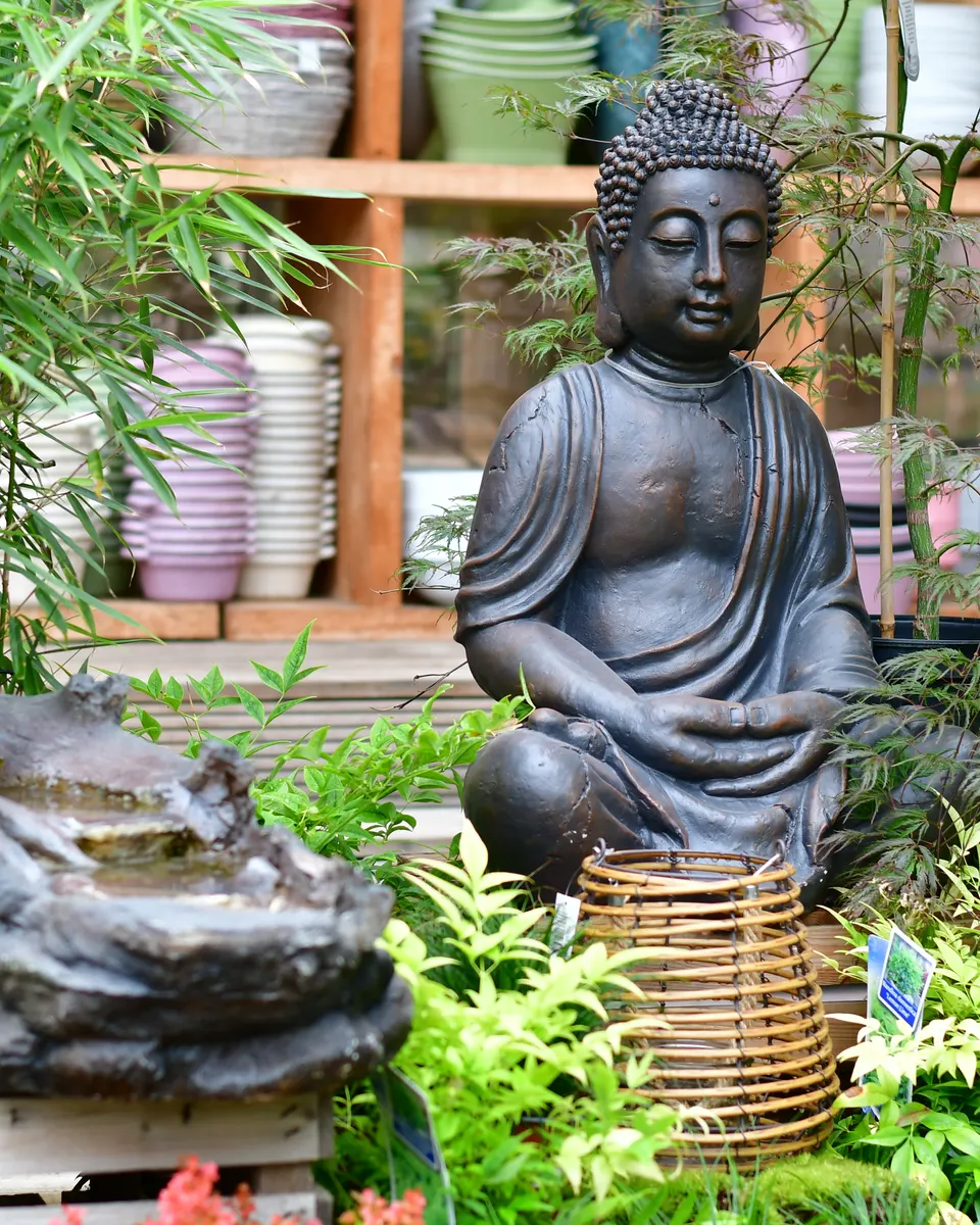 Buddha-Figur zwischen Pflanzen und kleinem Wasserlauf