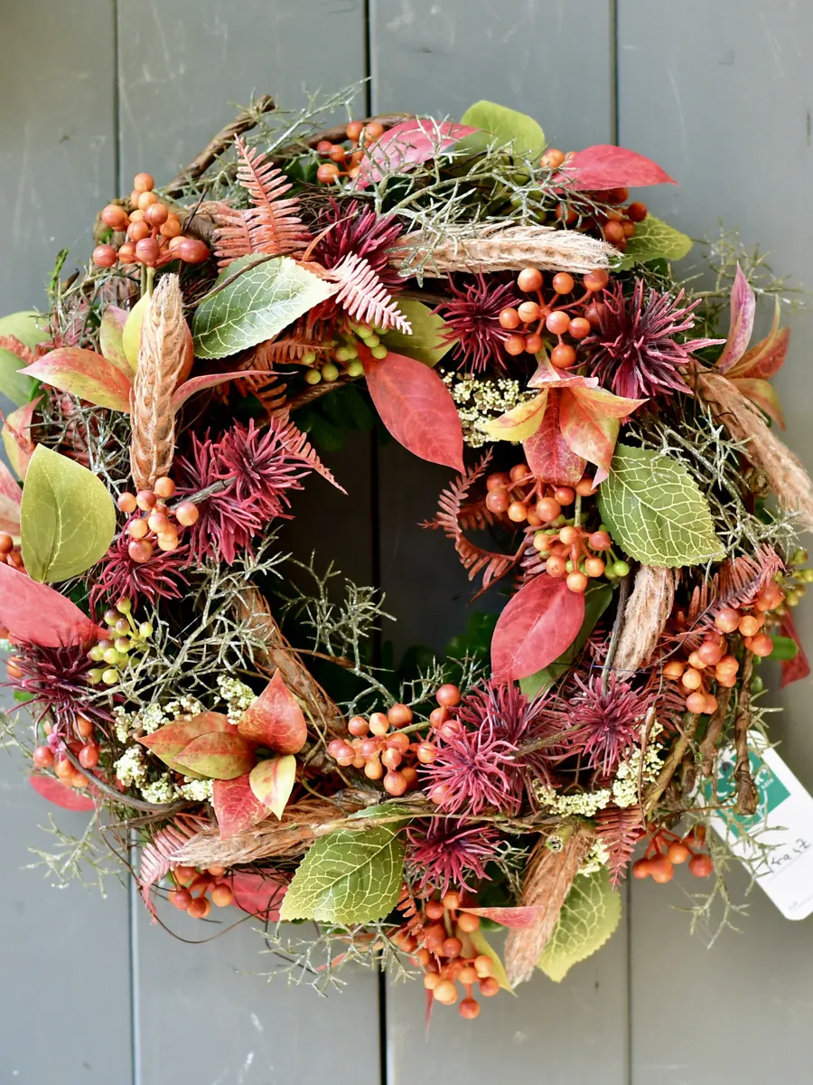 Herbstkranz mit Beeren und bunten Blättern an einer grauen Holzwand