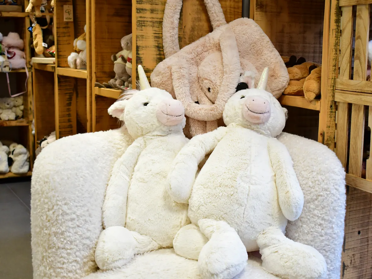 Zwei cremeweiße Einhorn-Kuscheltiere auf einem Sessel