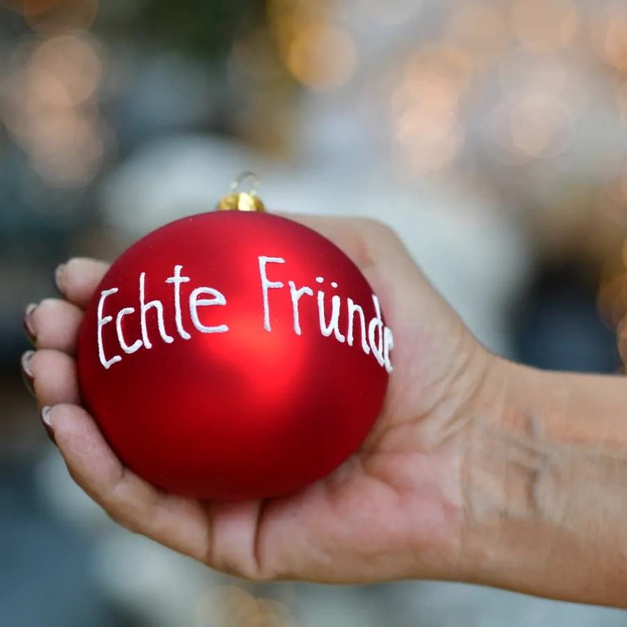 Rote Weihnachtskugel mit der Aufschrift Echte Fründe in einer Hand