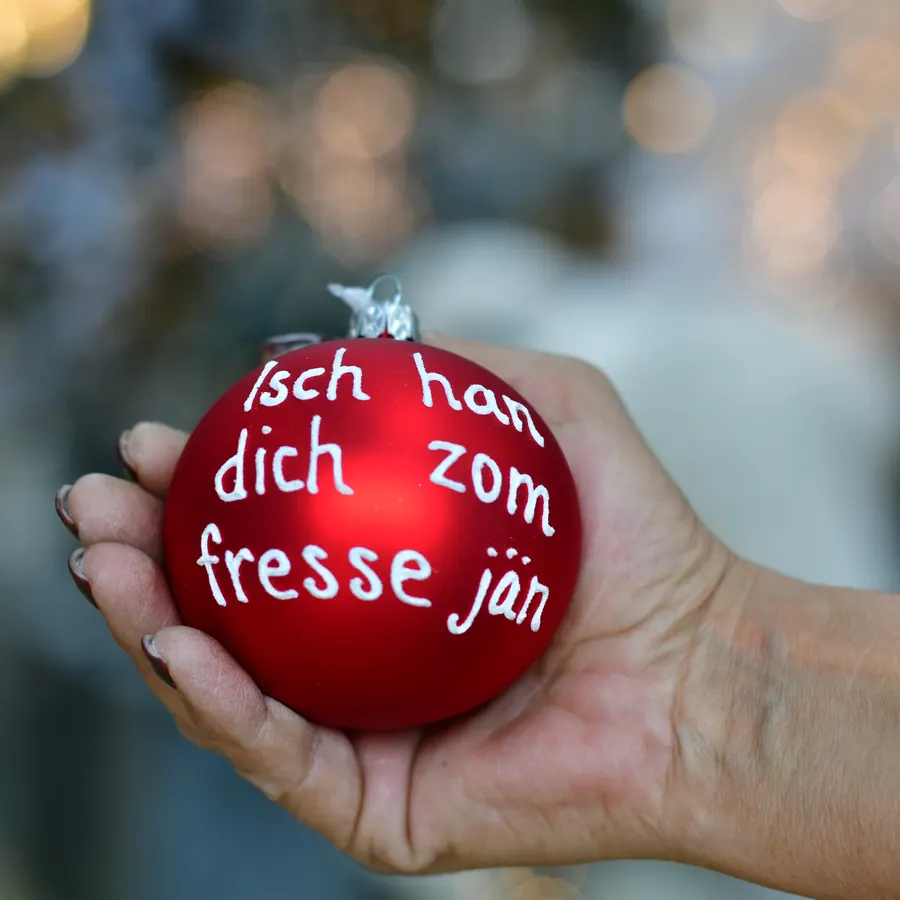 Rote Weihnachtskugel mit der Aufschrift Isch han dich zom fresse jän in einer Hand