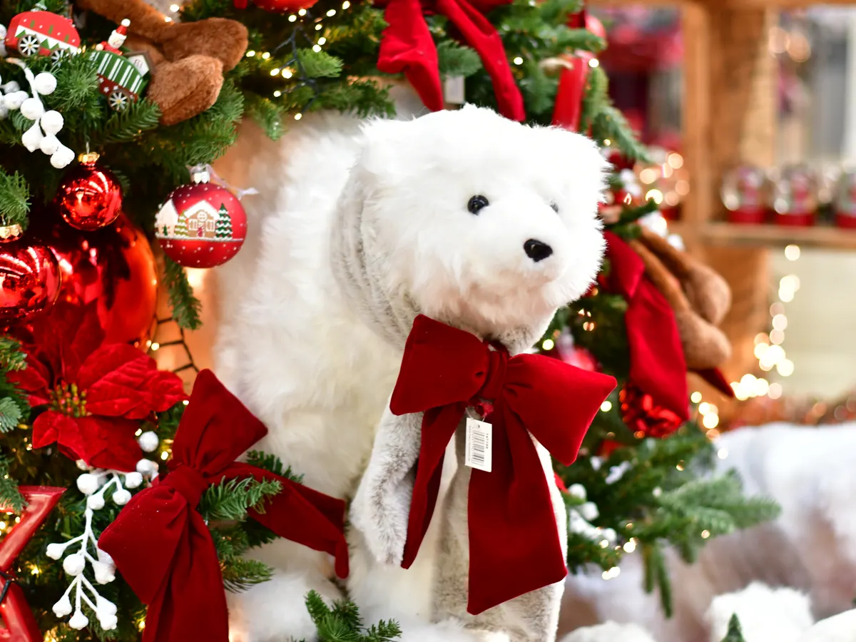 Plüsch-Eisbär mit roter Samtschleife zwischen Weihnachtsschmuck