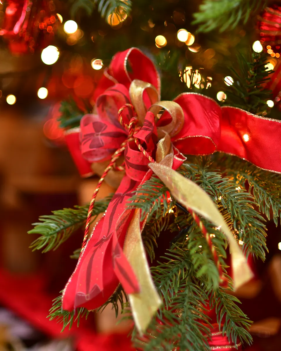 Handgebundene Schleife aus rotem und goldenem Band an einem beleuchteten Weihnachtsbaum